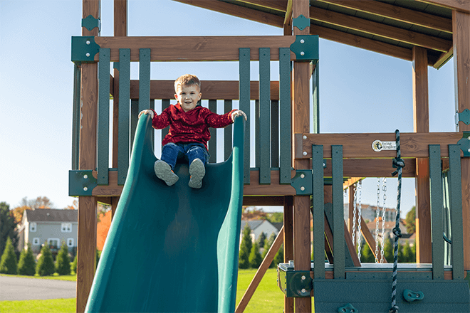 child sitting at the top of a playset slide