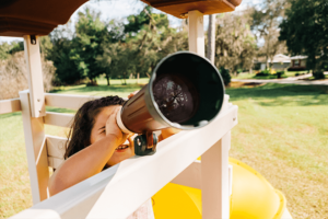 Girl looking out of a telescope attachment on a swing kingdom playset.