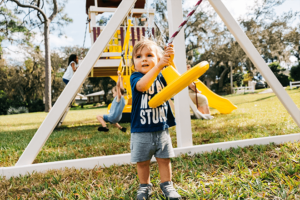 Little boy hanging on to a cyclone swing attachment on a playset.