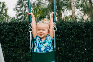 Little girl sitting in a bucket/baby swing on a playset.
