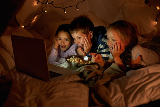 three kids in a fort watching a movie on a laptop