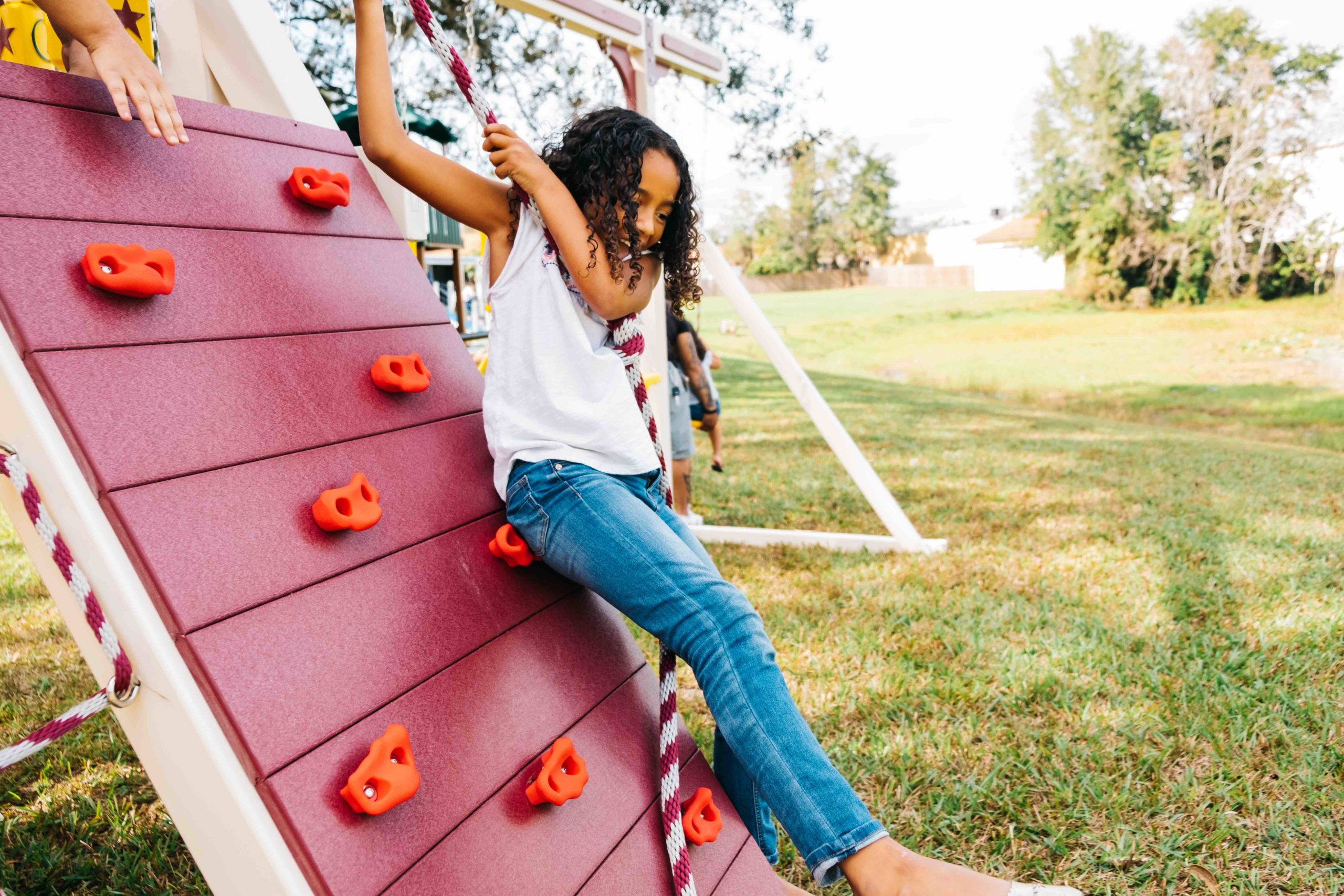 girl hanging on a rope attached to a rock wall on a playset