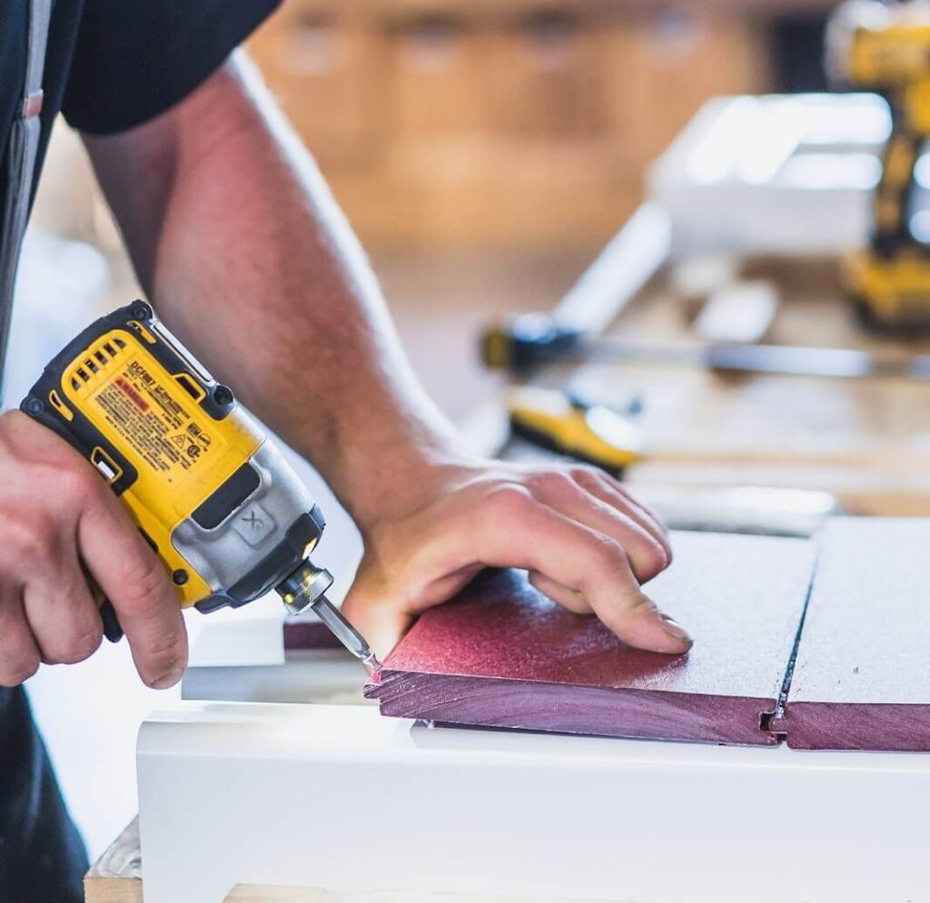 close up of a man using an electric drill to secure a piece of vinyl wood in place