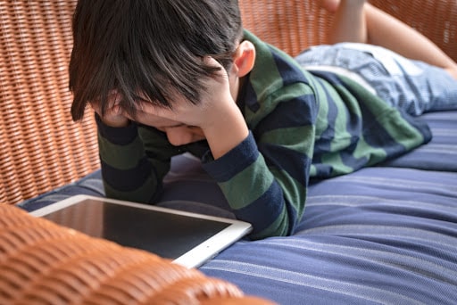 A young boy runs his hands through his hair, stressed out as he looks at a tablet.
