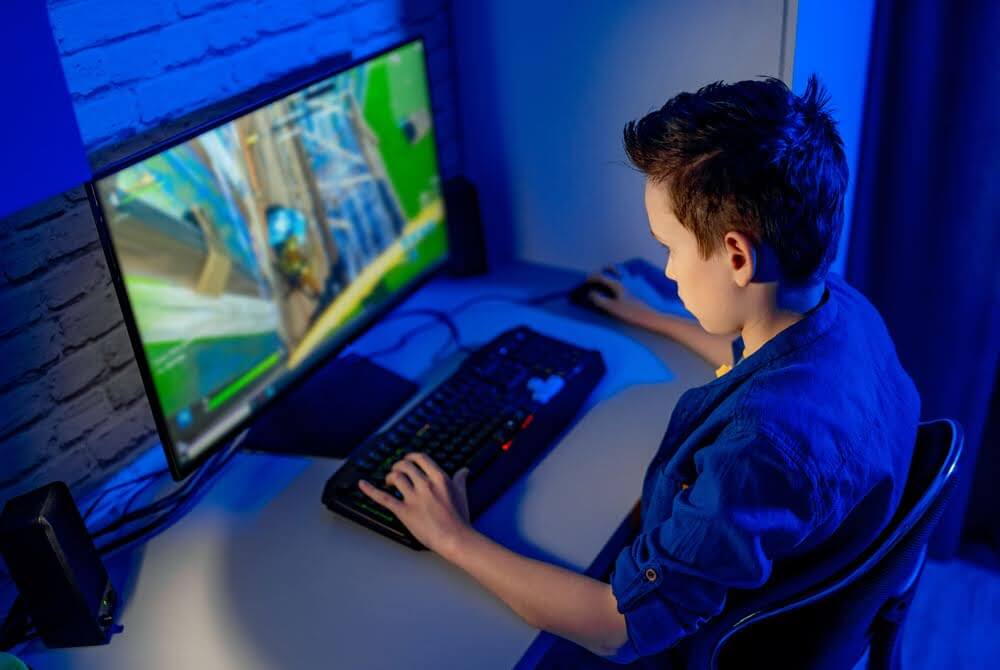 A young boy sitting in front of a computer screen focused in on playing a game.