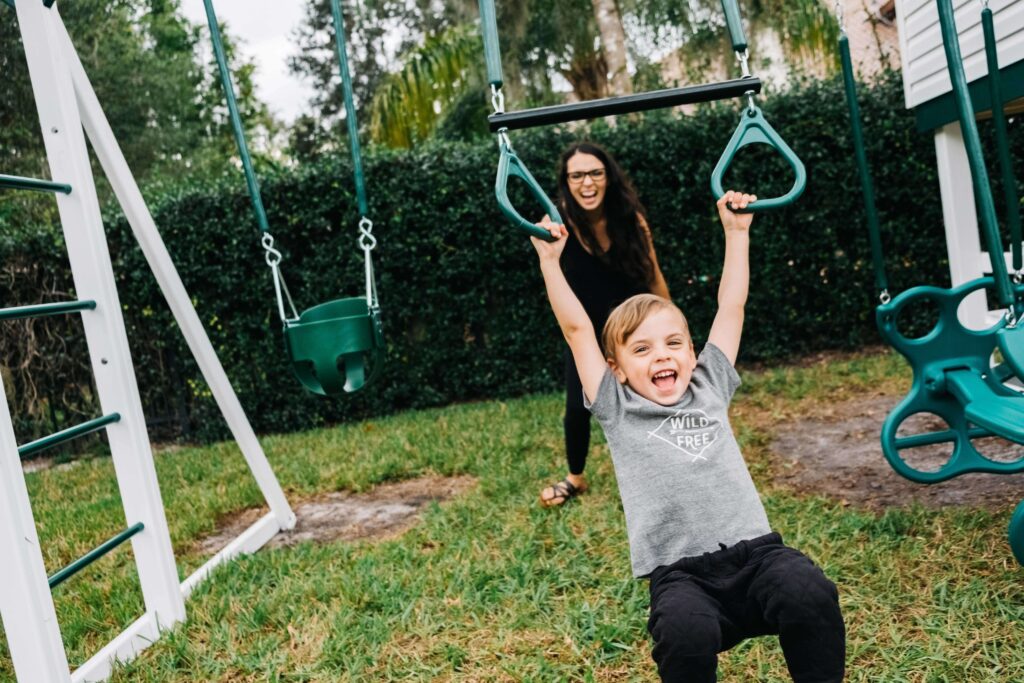 mother pushing son on playset trapeze bars