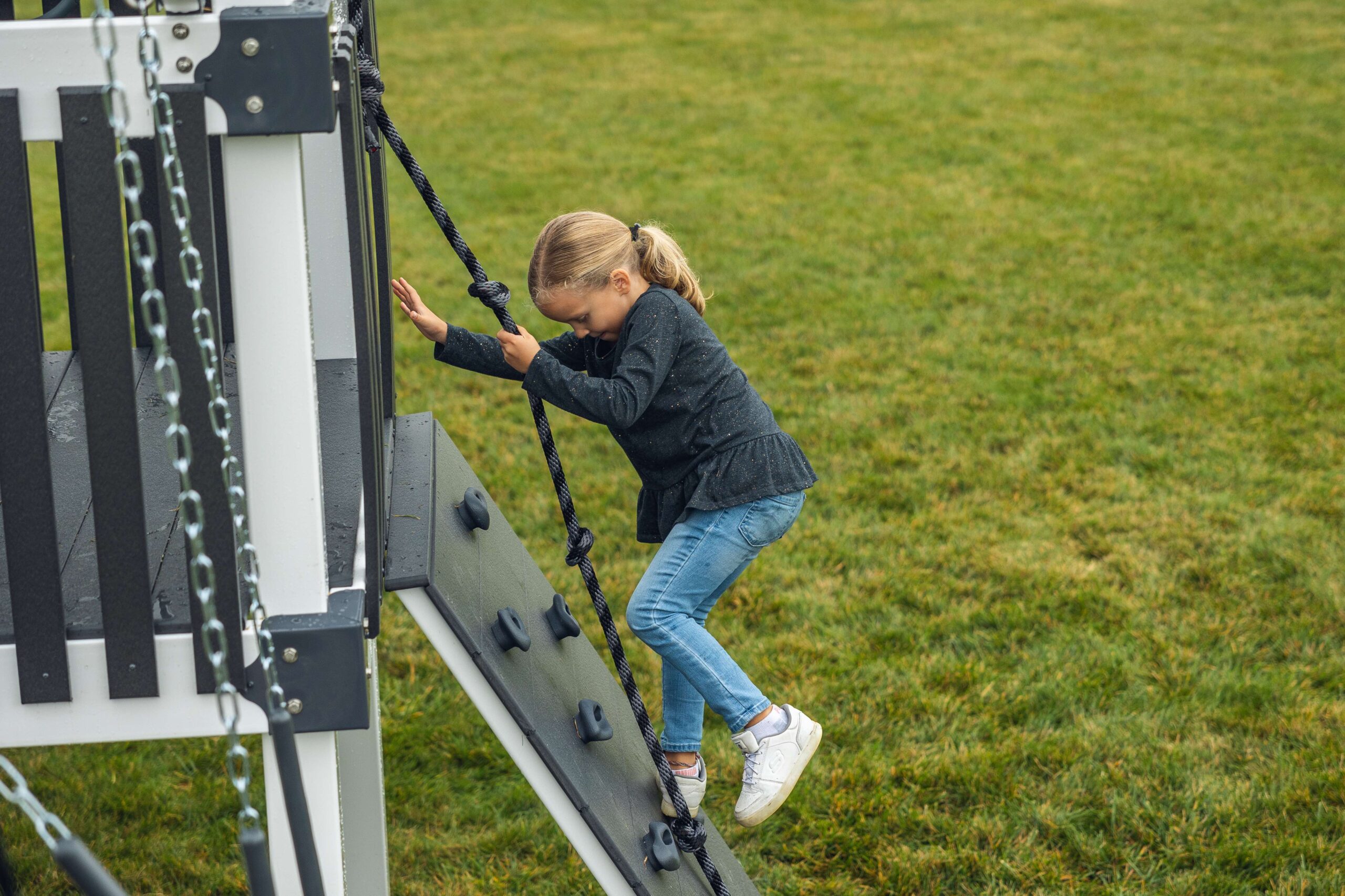 young girl climbing on a rock wall on a playset