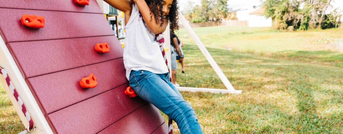 girl hanging on a rope attached to a rock wall on a playset