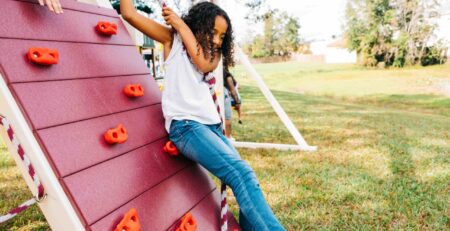 girl hanging on a rope attached to a rock wall on a playset